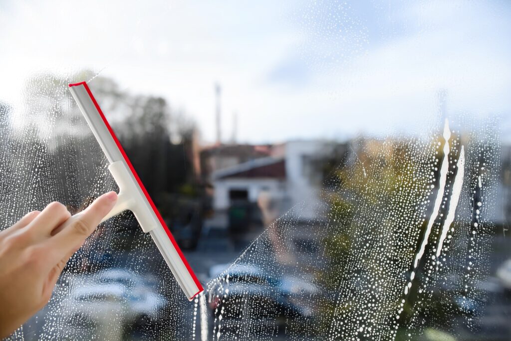 Glass cleaner with a squeegee for cleaning windows, blue sky. Person holds a squeegee in his hand